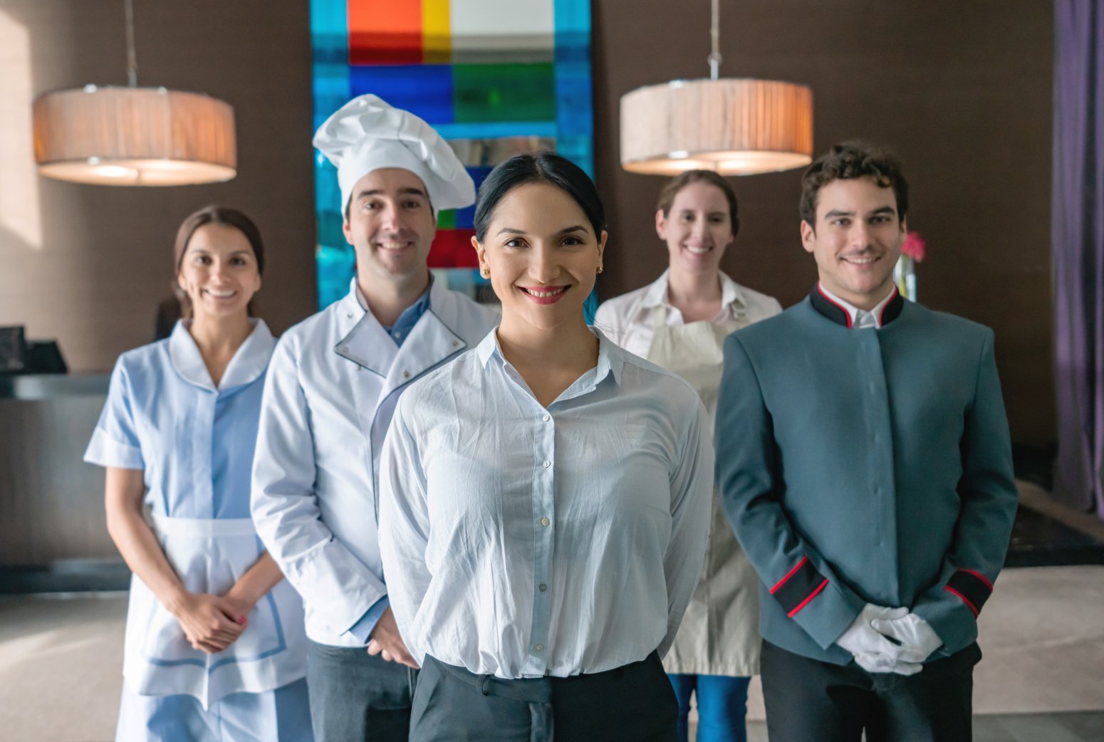 Portrait of cheerful luxury hotel staff smiling at camera and female supervisor standing at foreground